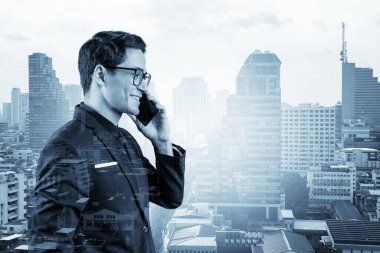 Takım elbiseli, gözlüklü, telefonla konuşan ve Bangkok 'un manzarasına bakan başarılı yakışıklı girişimci. Sorun çözme danışmanlığı kavramı. Şehir merkezi manzarası. Çift pozlama.