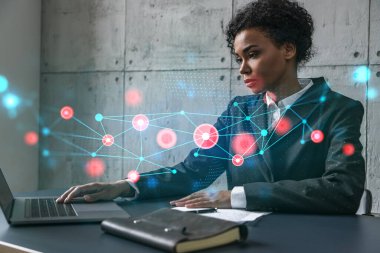Yeni bir proje için modern ofiste dizüstü bilgisayarla yazı yazan bir iş kadını. Soyut teknoloji ikonu hologram çiziyor. Çifte maruziyet. Başarı kavramı.