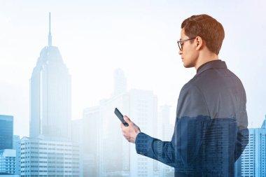 Takım elbiseli ve gözlüklü genç yakışıklı işadamı telefonla sorunu nasıl halledeceğini düşünüyor. Yeni kariyer fırsatları, işletme mastırı. Kuala Lumpur arka planda. Çift pozlama.