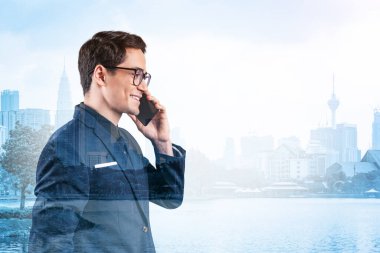 Takım elbiseli, gözlüklü, telefonla konuşan ve Kuala Lumpur şehri manzarasına bakan başarılı yakışıklı girişimci. Sorun çözme danışmanlığı kavramı. KL gökdelenleri. Çift pozlama.