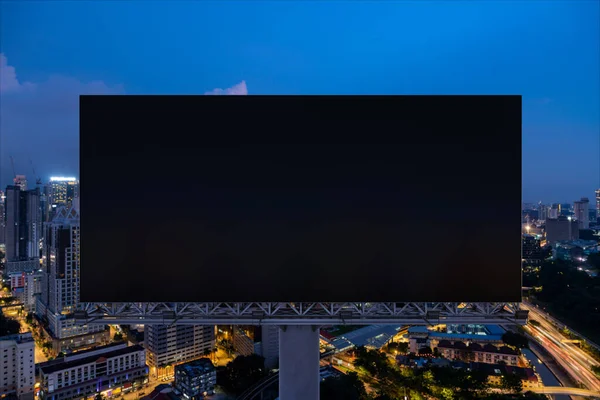 Blanco zwart wegreclamebord met Kuala Lumpur stadsgezicht achtergrond 's nachts. Reclameposter, model, 3D-weergave. Vooraanzicht. Begrip marketing om ideeën of producten te promoten of te verkopen. — Stockfoto