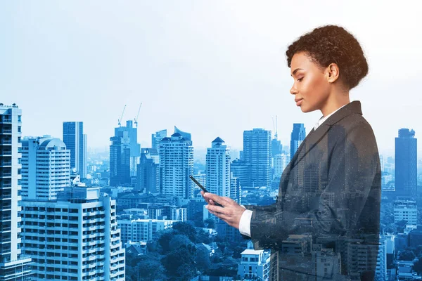 Привлекательная чернокожая афроамериканская деловая женщина в костюме, использующая смартфон и думающая, как решить проблему, новые карьерные возможности, MBA. Бангкок на заднем плане. Двойное воздействие. — стоковое фото