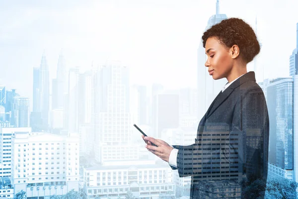Attractive black African American business woman in suit using smart phone and thinking how to tackle the problem, new career opportunities, MBA. Kuala Lumpur on background. Double exposure.