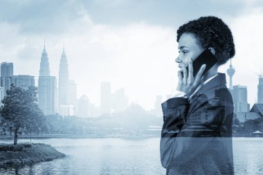 Başarılı gülümseyen, takım elbiseli siyahi, Afro-Amerikan iş kadını. Düşünceli konuşan telefon, Kuala Lumpur şehri. Sorun çözücü olarak danışman kavramı. KL gökdelenleri. Çift pozlama.