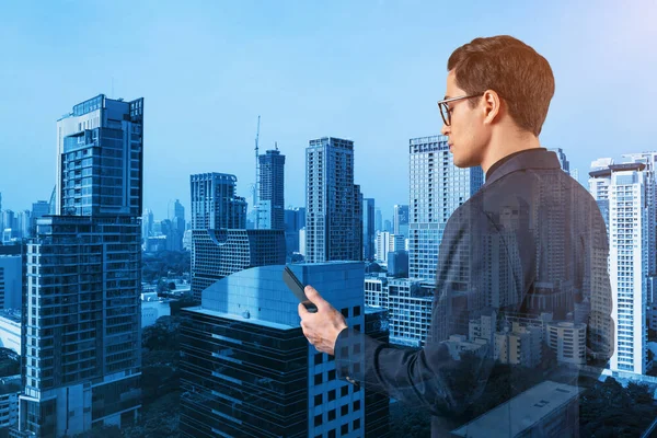 Young handsome businessman in suit and glasses using phone and thinking how to tackle the problem, new career opportunities, MBA. Bangkok on background. Double exposure.