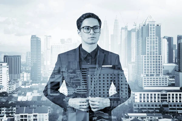 Joven hombre de negocios guapo en traje y gafas soñando con nuevas oportunidades de carrera después de la graduación del MBA. Kuala Lumpur en el fondo. Doble exposición. — Foto de Stock