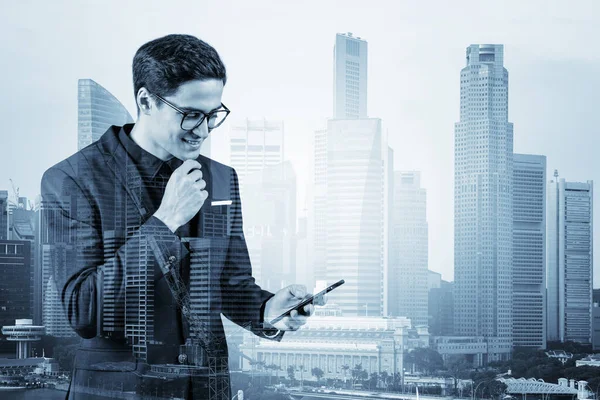 Young handsome businessman in suit and glasses using phone and thinking how to tackle the problem, new career opportunities, MBA. Singapore on background. Double exposure.