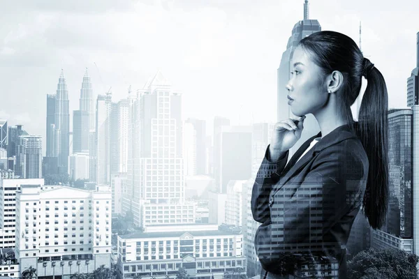 Привлекательная молодая азиатская деловая женщина в костюме с рукой на подбородке думает, как добиться успеха, новые карьерные возможности, MBA. Куала-Лумпур на заднем плане. Двойное воздействие. — стоковое фото