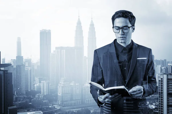 Young handsome businessman in suit and glasses thinking how to tackle the problem, new career opportunities, MBA assignment. Kuala Lumpur on background. Double exposure.