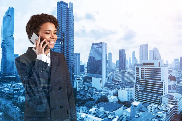 Успешная улыбающаяся чернокожая афроамериканская деловая женщина в костюме задумчиво разговаривающая по телефону, городской пейзаж Бангкока. Концепция консультантов как решателей проблем. Двойное воздействие. — стоковое фото