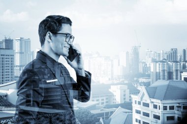 Takım elbiseli, gözlüklü, telefonla konuşan ve Kuala Lumpur şehri manzarasına bakan başarılı yakışıklı girişimci. Sorun çözme danışmanlığı kavramı. KL gökdelenleri. Çift pozlama.