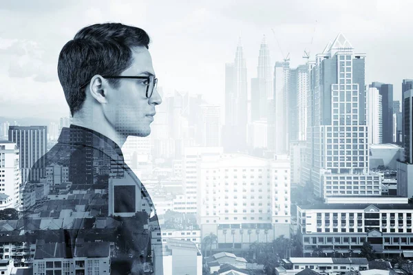 Takım elbiseli ve gözlüklü genç yakışıklı işadamı MBA mezuniyetinden sonra yeni kariyer fırsatları hayal ediyor. Kuala Lumpur arka planda. Çift pozlama.
