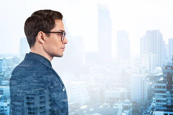 Takım elbiseli ve gözlüklü genç yakışıklı işadamı MBA mezuniyetinden sonra yeni kariyer fırsatları hayal ediyor. Bangkok arka planda. Çift pozlama.
