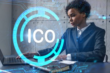 Yeni bir proje için modern ofiste dizüstü bilgisayarla yazı yazan bir iş kadını. ICO simgesi hologram çiziyor. Çifte maruziyet. Başarı kavramı.