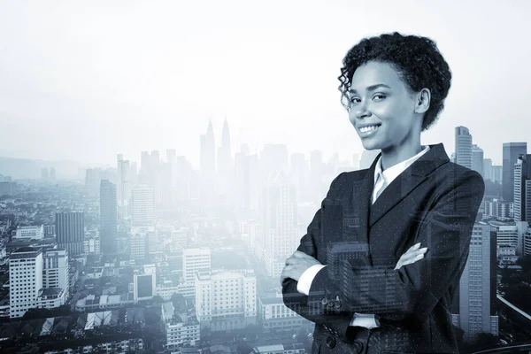Smiling black African American business woman in suit in crossed arms pose. Kuala Lumpur cityscape. The concept of woman in business. KL skyscrapers. Double exposure.