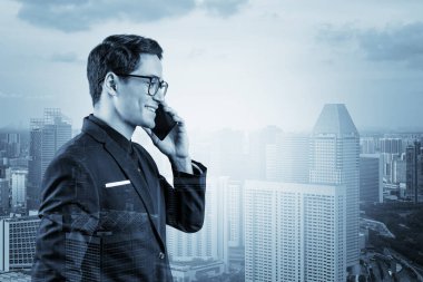 Takım elbiseli ve gözlüklü başarılı yakışıklı girişimci sürekli telefonla konuşuyor ve Singapur şehir manzarasına bakıyor. Sorun çözme danışmanlığı kavramı. Şehir merkezi manzarası. Çift pozlama.