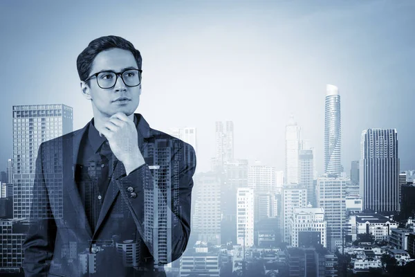 Joven hombre de negocios guapo en traje y gafas soñando con nuevas oportunidades de carrera después de la graduación del MBA. Bangkok en el fondo. Doble exposición. — Foto de Stock