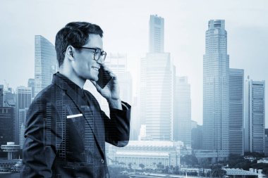 Takım elbiseli ve gözlüklü başarılı yakışıklı girişimci sürekli telefonla konuşuyor ve Singapur şehir manzarasına bakıyor. Sorun çözme danışmanlığı kavramı. Şehir merkezi manzarası. Çift pozlama.