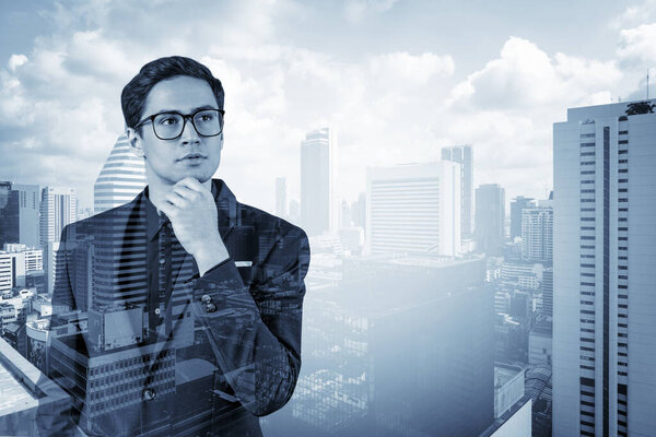 Young handsome businessman in suit and glasses dreaming about new career opportunities after MBA graduation. Bangkok on background. Double exposure.