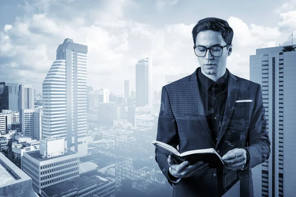 Joven hombre de negocios guapo en traje y gafas pensando en cómo abordar el problema, nuevas oportunidades de carrera, asignación de MBA. Bangkok en el fondo. Doble exposición. — Foto de Stock