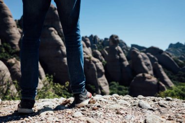 Çocuk bir dağın tepesinde manzaraya bakıyor.