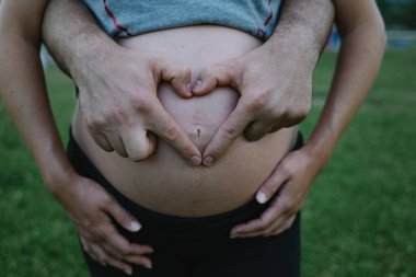 Koca, karısının hamile karnında parmaklarıyla kalp şekli yaratıyor.