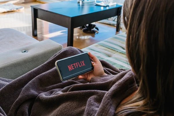 Kız kanepede battaniyeyle kaplanmış cep telefonundan Netflix izliyor..