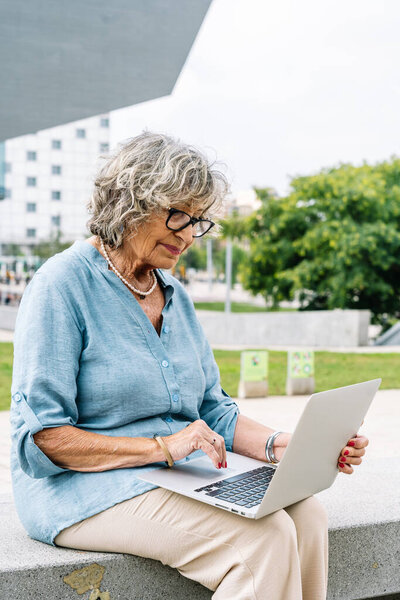 Senior woman enjoying working remotely on laptop computer outdoors