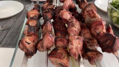 Lezzetli bir kızarmış kebap, şampanya ve şarap, taze sebzeler ve otlar, pide ekmeği ve sebze salatası olan bir masa..