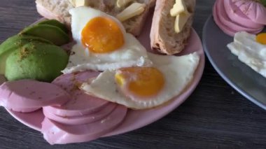 Tabakta kahvaltı. Yağda yumurta, ekmek ve tereyağı, avokado ve sosis.