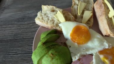Kahvaltı için iki sahanda yumurta, sosis, avokado, ekmek ve tereyağlı.