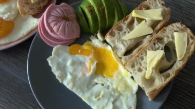 İki kişi için lezzetli ve doyurucu bir kahvaltı. Sahanda yumurta, ekmek, sosis ve avacado.
