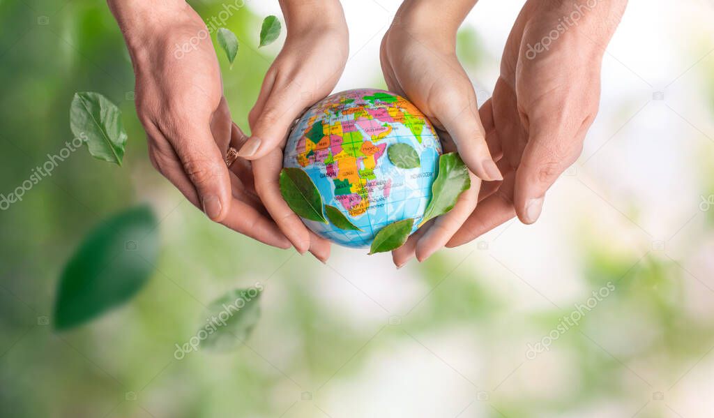 Male and female hands holding the earth on a background of green leaves and spring summer background. Save planet, economical consumption, eco, ecology. Symbolic of peaceful and safe the Earth.