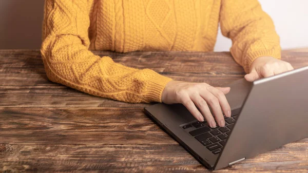 A woman in a yellow sweater works, studies on a laptop at a wooden table at home. Concept of quarantine, remote work at home, distance learning students, business, freelancer, freelance, SMM Manager
