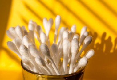 Sarı arka planda pamuklu çubuklar. Yakın plan. Güneşin ışınları perdelerin ardında. Kulakların hijyeni. Makyaj Düzeltme