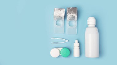 Kontakt lensler ayarlandı. Şişede tuz, cımbız, göz damlası, mavi arka planda çözeltisi olan plastik kutu..