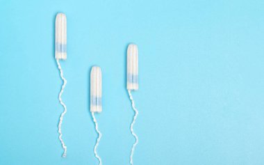 Mavi arka planda üç adet tamponu. Adet döngüsü. Hijyen ve koruma. Tek kullanımlık tampon. Adet öncesi.