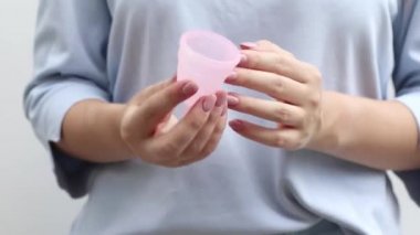 Adet bardağının nasıl kullanılacağını. Kadın, tıbbi silikondan yapılmış regl eko bardağının nasıl çöktüğünü gösteriyor. Video talimatı. Yakın çekim, sıfır atık.