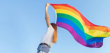 Lezbiyenleri tutan bir kadın açık havada gökyüzünde gökkuşağı bayrağı taşıyor. Aynı cinsiyet çiftleri için mutluluk ve aşk kavramı. Dışarıda yaşam tarzı. Lisbian 'lı genç bayan kopyalama alanı ile bayrak sallıyor Gurur ayı