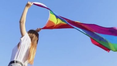 Genç bir kadın, LGBT topluluğunu desteklemek için gökyüzüne karşı gökkuşağı bayrağı dikiyor. Özgür aşk kavramı, hakların eşitliği, lezbiyen, LGBTQI, Gurur Etkinliği, LGBT Onur Ayı. Ukraynalı kadın