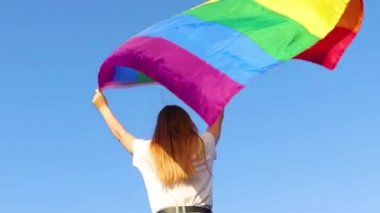 Genç bir kadın, LGBT topluluğunu desteklemek için gökyüzüne karşı gökkuşağı bayrağı dikiyor. Özgür aşk kavramı, hakların eşitliği, lezbiyen, LGBTQI, Gurur Etkinliği, LGBT Onur Ayı. Ukraynalı kadın.