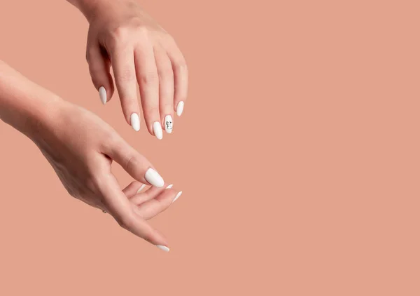 Hands of a beautiful well-groomed woman with feminine nails on a beige background. Manicure, pedicure beauty salon concept. Empty space for text or logo. On nails white gel polish with an abstract.