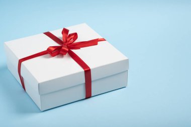 Beyaz arka planda kırmızı kurdeleli beyaz hediye kutusu ve fotokopi alanı. Minimalist kompozisyon. Evrensel tatil konsepti, Anneler Günü, Sevgililer Günü, Noel, Yeni Yıl, Doğum günü, indirim