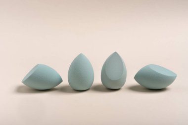 Bej rengi çıplak arka planda mavi makyaj yumurtası süngeri. Farklı şekillerde süngerler. Temeli uygulamak için araç. Kimse..