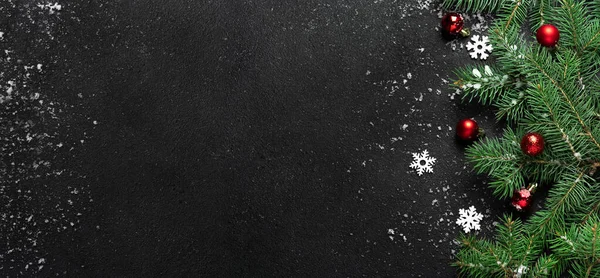 Noel ya da yeni yıl dekorasyon afişi. Köknar ağacı dalları için fotokopi alanı olan siyah arkaplan. Düz yatıyordu. Şablon. Beyaz kar taneleri ve kar, kırmızı toplar