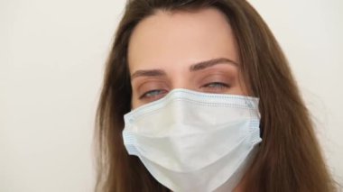 Maskeli kızın yüzünü yaklaştır. Genç kadın gözleriyle farklı duygular gösteriyor, yüzü tıbbi bir maske tarafından gizleniyor. Kadın kaşlarını oynatıyor.