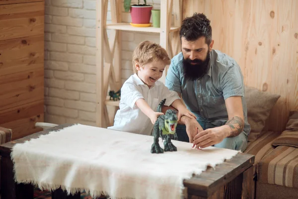 A happy family is played with dinosaurs. The son and father play at home. A bearded man entertains his son. A boy with toys together with his father. Friendship with parent and entertainment