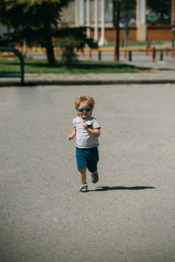 Güneş gözlüklü çocuk yol boyunca çalışır. Koşucu. Çocukluk şehir. Çekici şık çocuk. Mutlu bir çocuk tatilde çalışıyor. Summer, dinlenme, çocuklar spor