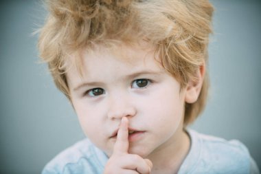 Boy with finger on lips making a silent gesture. Please be quiet. Smart cute young boy with his finger over his lips being quiet. Little boy showing silence symbol gesture. Secret young kid guy clipart