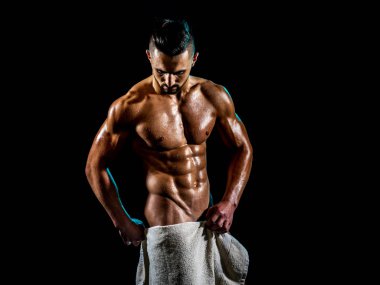 Naked handsome young man with perfect body and tanned skin against black. Attractive muscular bodybuilder hold towel and wears no underwear. Man after bath. clipart